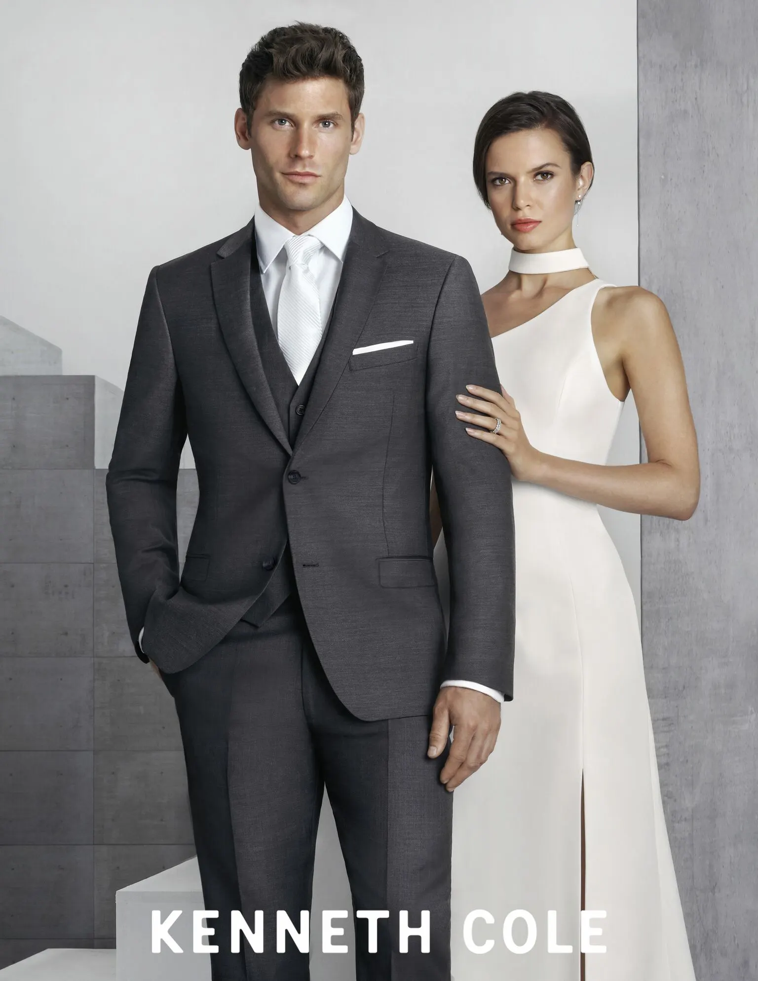 man wearing black three piece suit and white tie, woman wearing white dress and matching choker